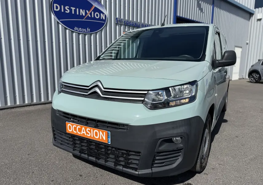 Vue 3/4 avant droit d’un Citroën Berlingo beige 2019 avec pare-chocs noir et plaque orange « OCCASION » devant un bâtiment industriel.