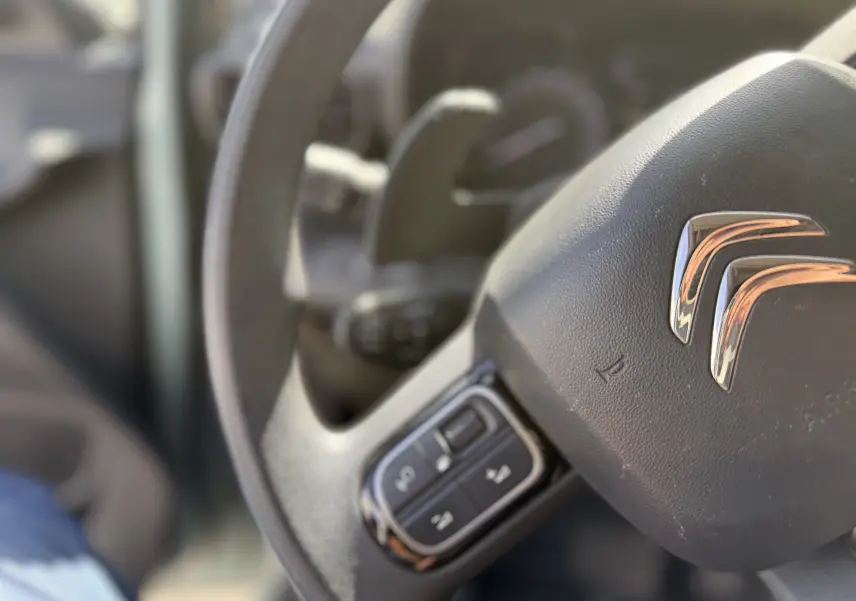 Gros plan sur le volant noir avec commandes intégrées du Citroën Berlingo FGN 2019, intérieur beige flouté en arrière-plan.