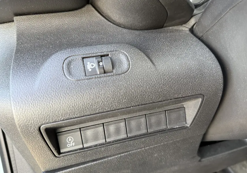 Gros plan sur les commandes noires côté gauche du tableau de bord du Citroën Berlingo beige, avec réglage des phares et bouton arrêt auto start-stop.