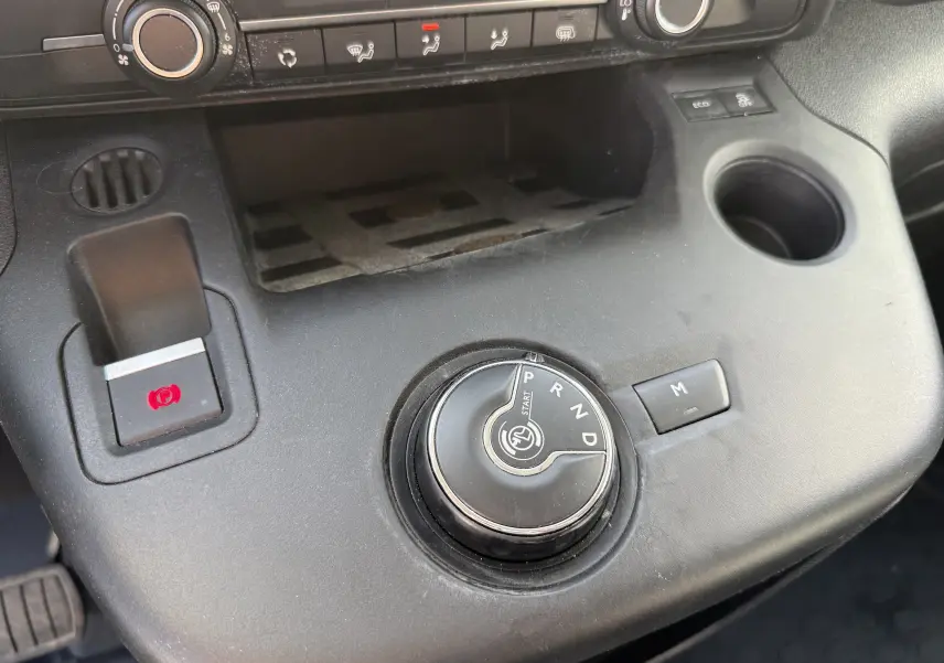 Gros plan sur la console centrale noire du Citroën Berlingo beige, avec molette de boîte auto et bouton de frein à main électrique.