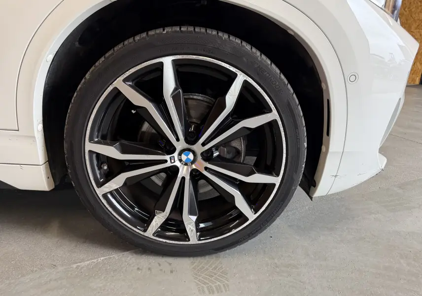 Gros plan sur la roue avant droite d'une BMW X2 blanche avec jante alu 19'' bicolore et logo BMW central.