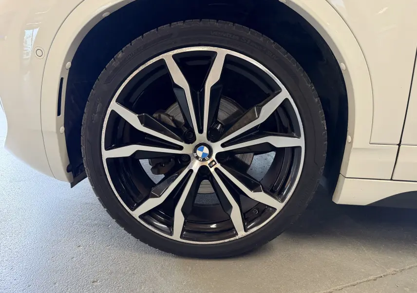 Gros plan sur la jante alu 19 pouces bicolore noire et argentée du côté arrière droit d'un BMW X2 blanc.