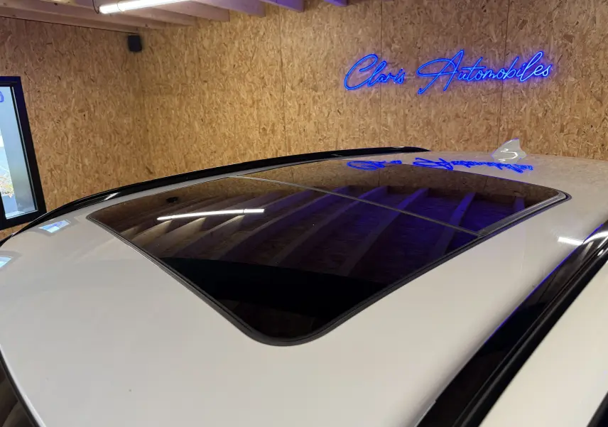 Toit ouvrant panoramique en verre sur BMW X2 blanc, vue en plongée depuis l'arrière droit dans un garage.