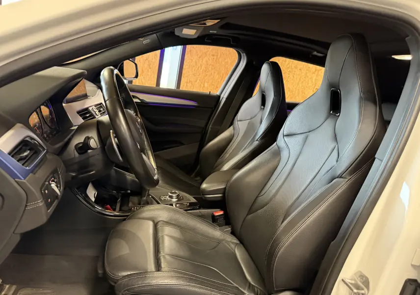 Vue intérieure côté conducteur d'une BMW X2 sDrive18d 2023 avec sièges sport cuir noirs et toit ouvrant panoramique.