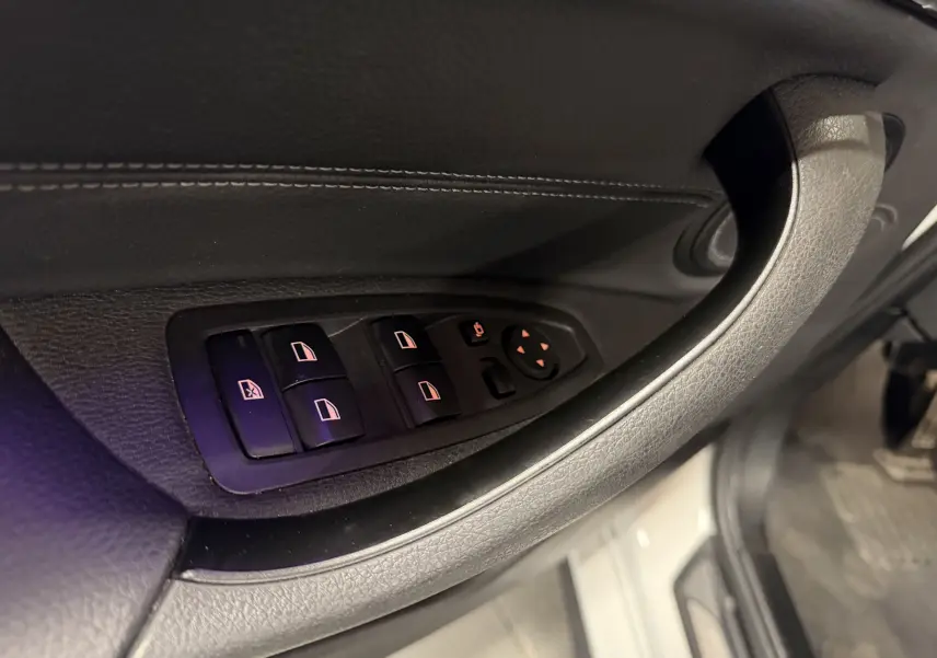 Gros plan sur les commandes électriques des vitres et rétroviseurs sur la porte côté conducteur d’une BMW X2 blanche.