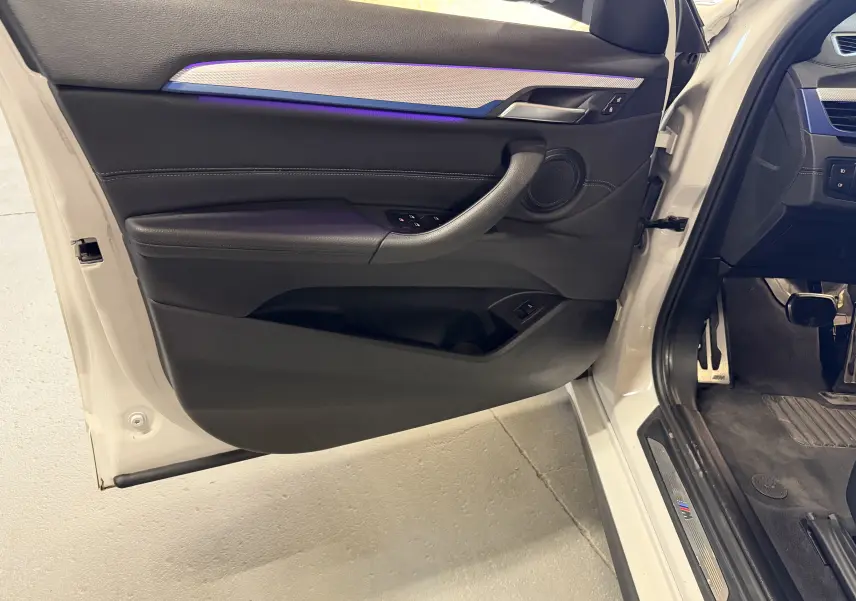 Vue intérieure de la porte avant gauche blanche d’un BMW X2 2023 avec éclairage d’ambiance violet et garniture noire.