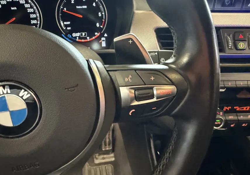 Gros plan sur le volant cuir multifonctions noir d'une BMW X2 sDrive18d 2023 avec palettes au volant et tableau de bord digital.