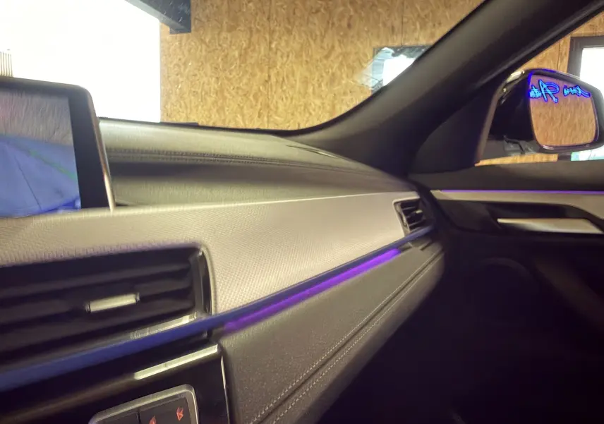 Vue intérieure côté passager du tableau de bord noir avec éclairage d'ambiance violet d'un BMW X2 sDrive18d 2023.