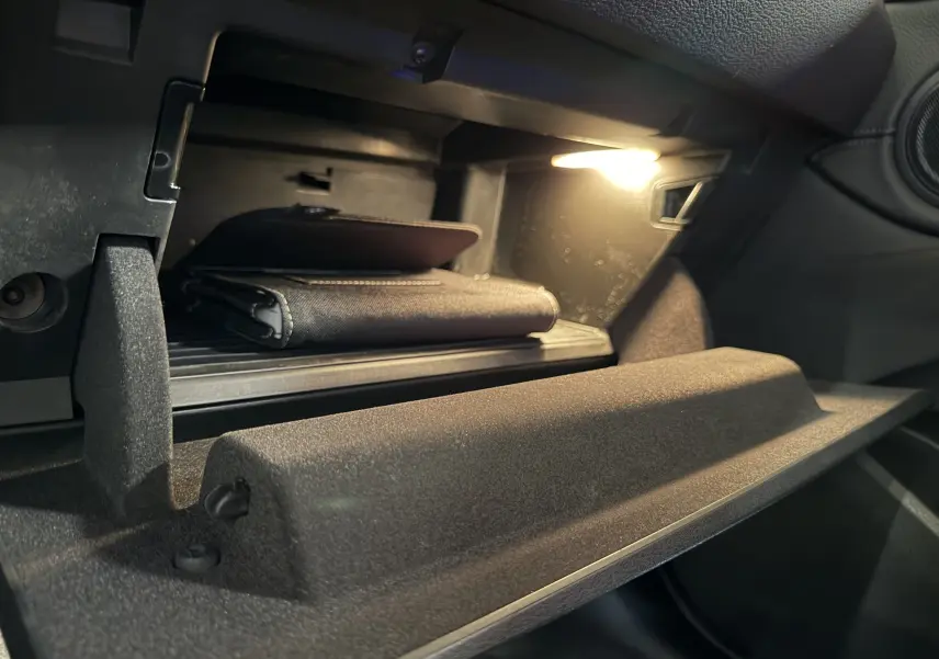 Vue rapprochée de la boîte à gants ouverte du BMW X2 blanc 2023, éclairée avec un manuel à l'intérieur.