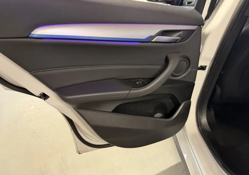 Vue intérieure de la porte arrière droite d'une BMW X2 blanche avec éclairage d'ambiance violet et garniture noire.