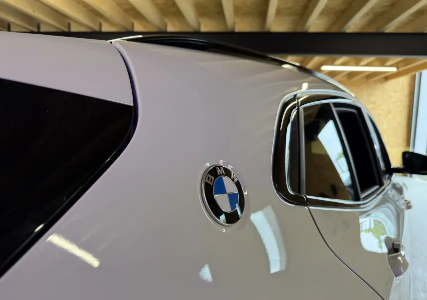 Vue latérale droite rapprochée d’un BMW X2 blanc avec logo BMW sur le montant arrière et vitres teintées.