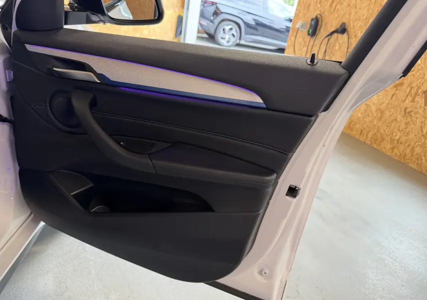 Vue intérieure de la porte avant gauche blanche du BMW X2 2023 avec éclairage d'ambiance bleu et garniture noire.