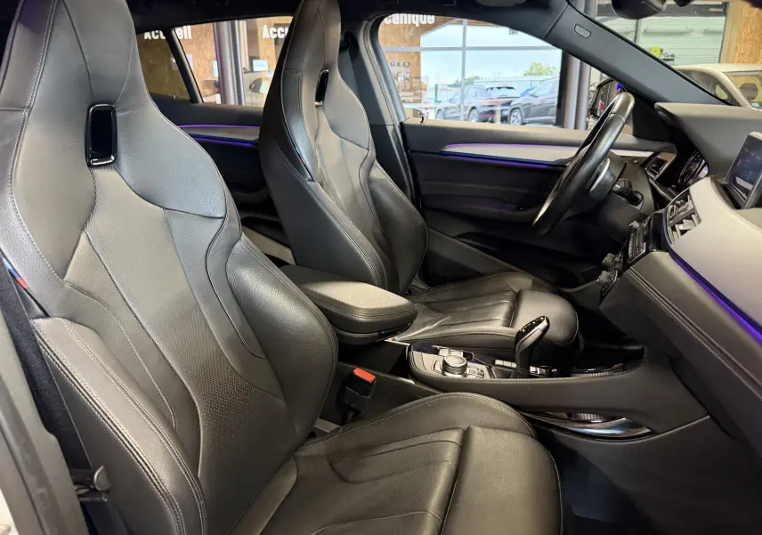 Vue intérieure côté droit de la BMW X2 sDrive18d 2023 avec sièges sport cuir noirs et éclairage d’ambiance violet.