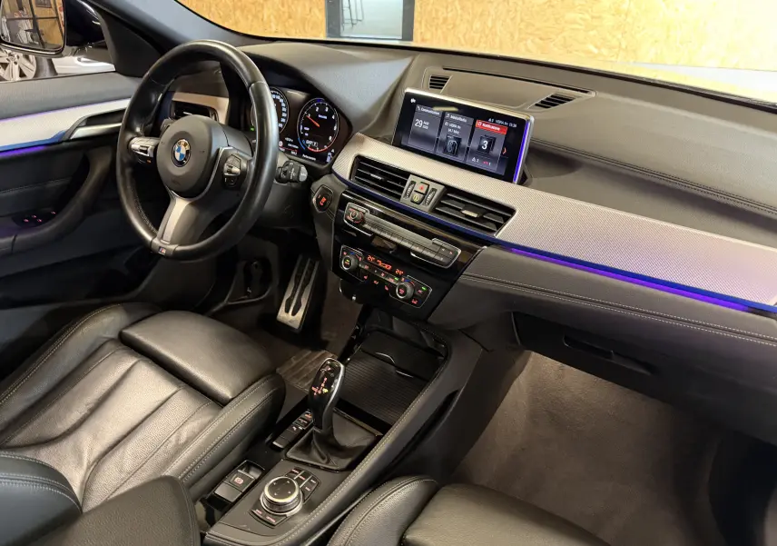 Vue intérieure côté conducteur de la BMW X2 sDrive18d 2023, avec tableau de bord noir et écran central lumineux.