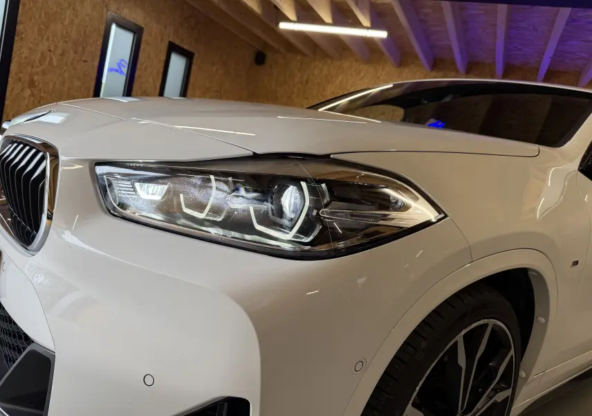 Gros plan sur l'avant droit blanc du BMW X2 2023 avec phares LED et jantes alu 19 pouces en intérieur.