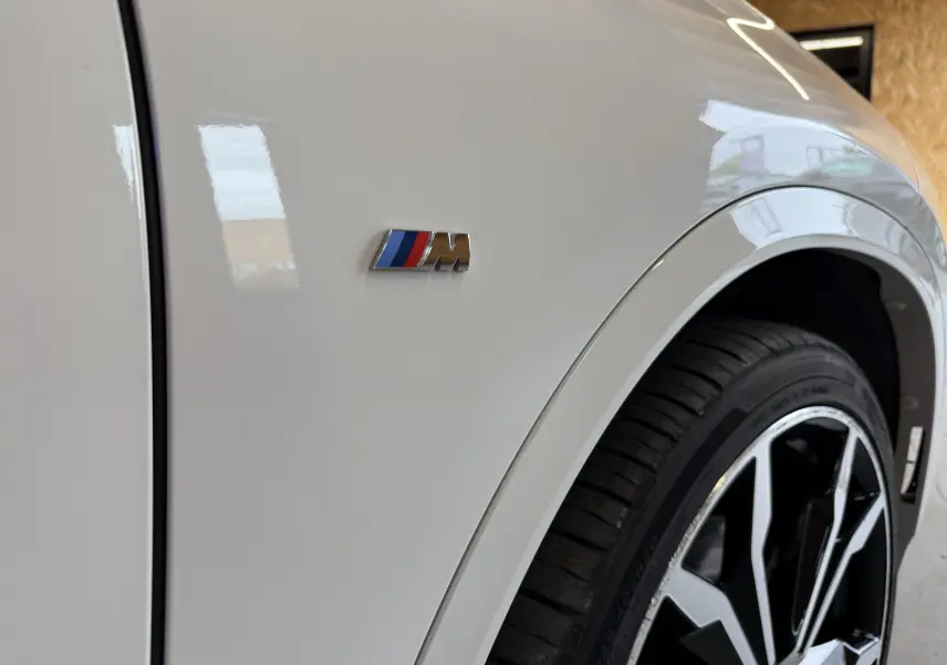 Gros plan sur l'aile avant droite blanche d'une BMW X2 avec logo M et jante alu noire et argentée.