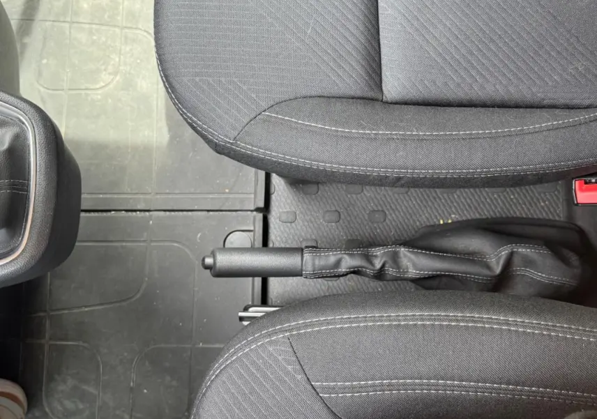 Vue intérieure centrée sur le frein à main entre les sièges avant en tissu gris foncé du Renault Trafic Fourgon 2024.