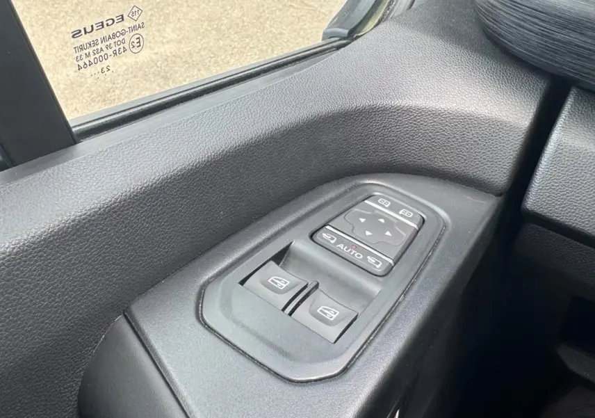 Gros plan sur les commandes électriques des vitres et rétroviseurs côté conducteur du Renault Trafic Fourgon gris foncé 2024.
