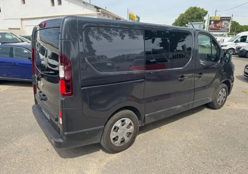Renault Trafic Fourgon gris foncé vu en 3/4 arrière droit, avec porte latérale et vitres surteintées.