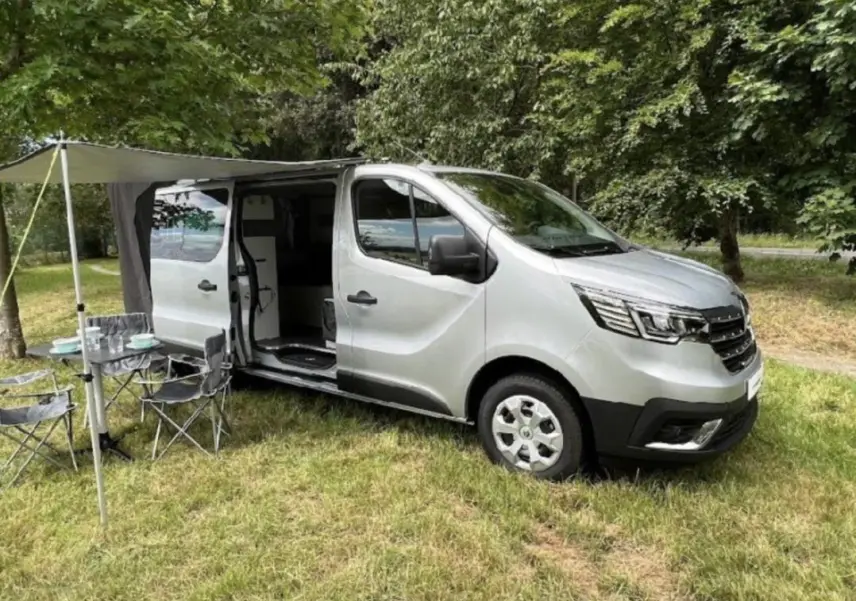 Vue 3/4 avant droit d'un Renault Trafic Fourgon gris foncé avec porte latérale ouverte et auvent déployé.