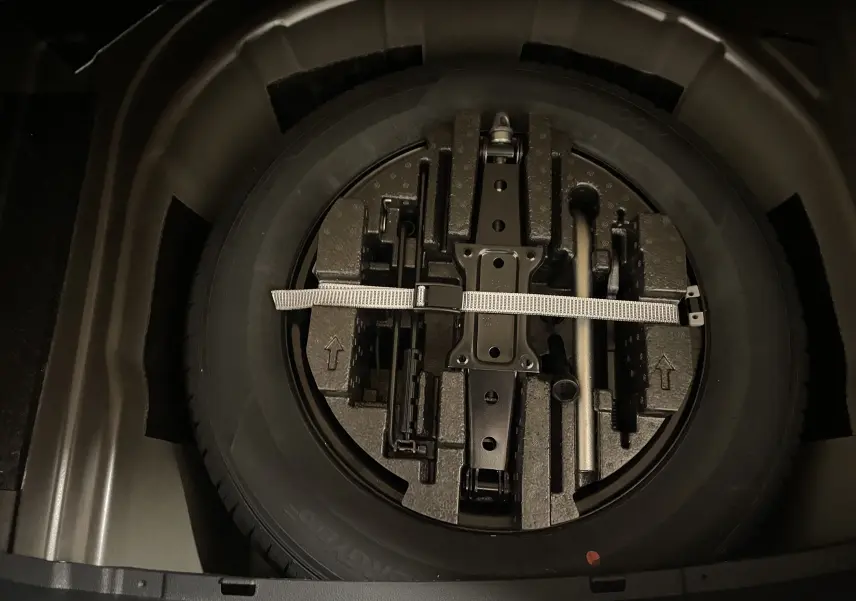 Gros plan sur la roue de secours et les outils de bord dans le double plancher du coffre du Skoda Scala Noir Magic.