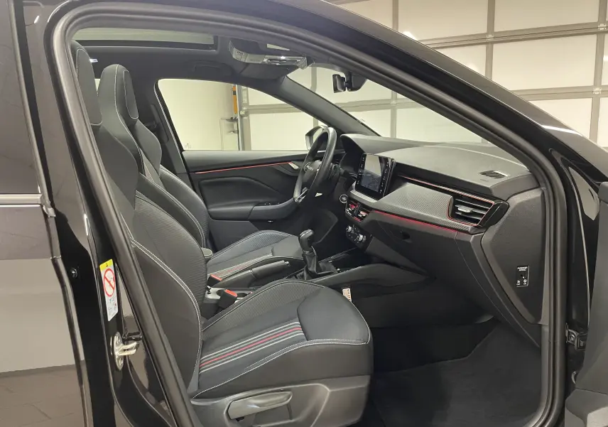 Vue intérieure côté gauche de la Skoda Scala 1.5 TSI 2025 noire avec sièges sport et bandeaux rouges décoratifs.