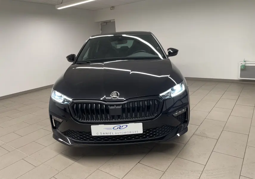 Vue avant d'une Skoda Scala 1.5 TSI Monte-Carlo en noir Magic avec phares allumés dans un showroom.