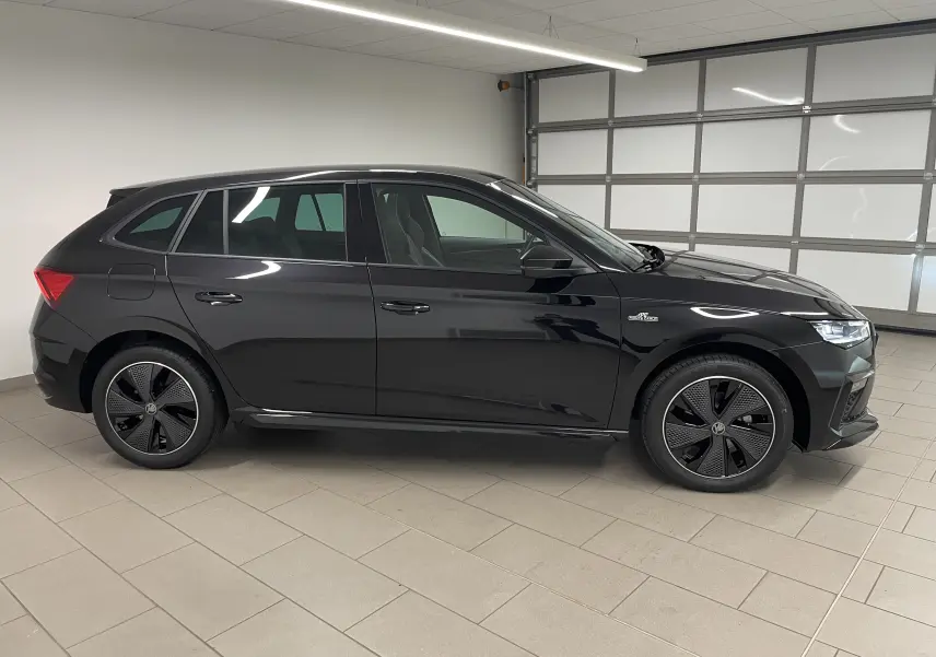 Vue de profil côté gauche d'une Skoda Scala 1.5 TSI 150 DSG7 Monte-Carlo noire métallisée avec jantes spécifiques en intérieur fermé.