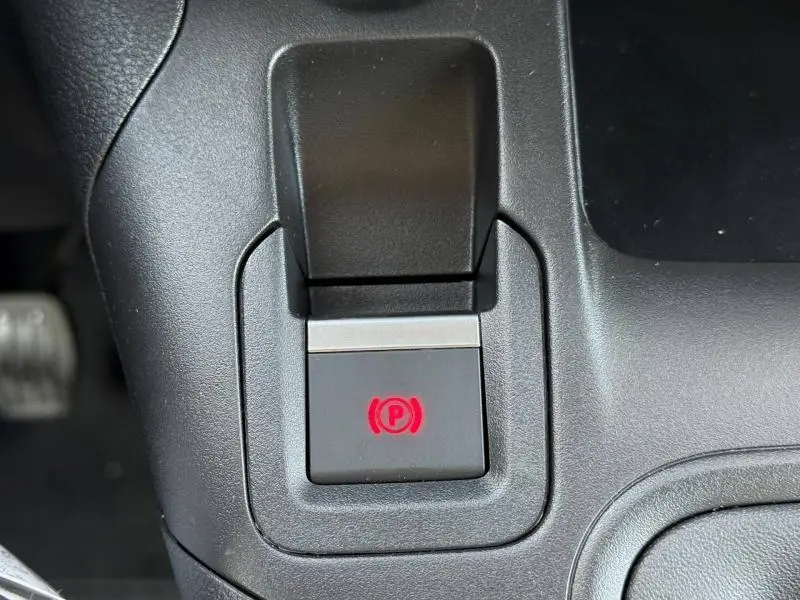 Gros plan sur le bouton de frein à main électronique rouge dans l'habitacle noir du Citroën Berlingo 2025.