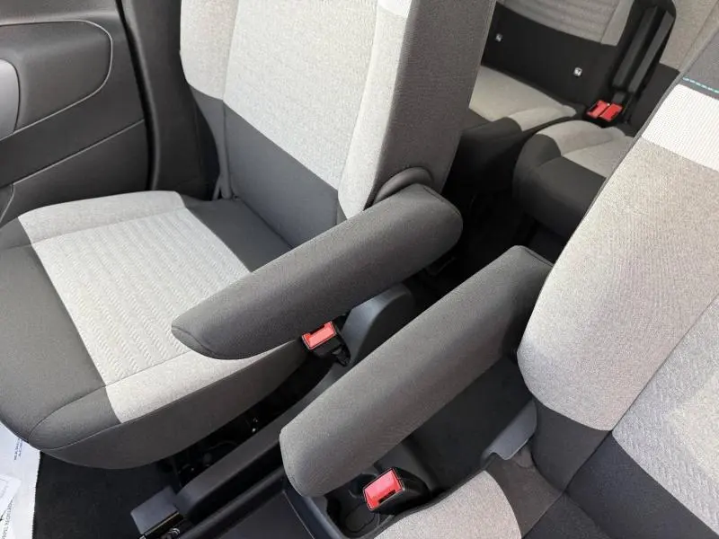 Gros plan sur les sièges avant gris clair et foncé du Citroën Berlingo 2025 avec accoudoirs centraux relevés.