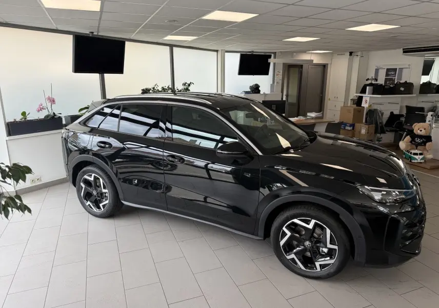 Volkswagen T-Roc R-Line noir intense en vue 3/4 avant droit, avec jantes alliage et vitres teintées, dans un showroom.