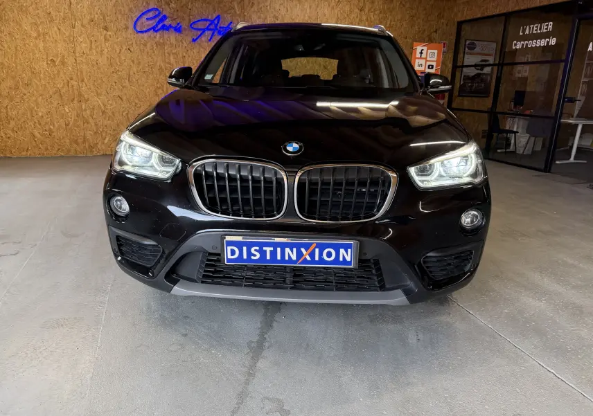 Vue de face d’un BMW X1 noir (F48) 2019 avec calandre double haricot et phares allumés en intérieur.