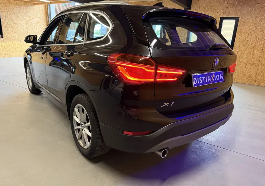 BMW X1 noir vue 3/4 arrière droit dans un garage, feux arrière allumés et logo X1 visible sur le hayon.