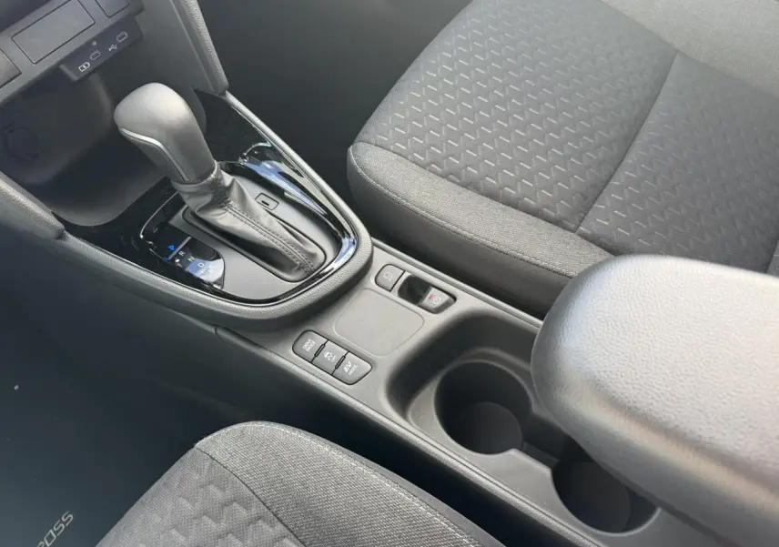 Gros plan intérieur sur la console centrale et levier de vitesse de la Toyota Yaris Cross 1.5 Hybrid gris avec sièges tissu gris.