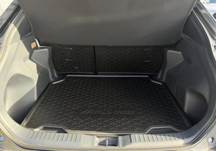 Coffre ouvert d'une Toyota Yaris Cross 1.5 Hybrid 130 BVA Design gris, avec tapis de coffre noir marqué Yaris Cross.