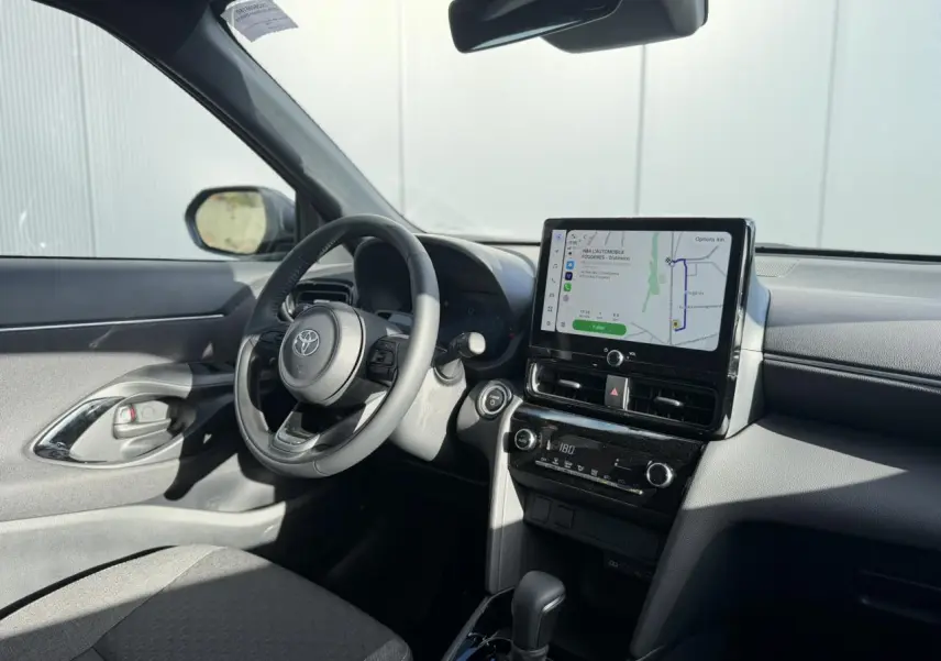 Intérieur de la Toyota Yaris Cross 2026 en gris, vue côté conducteur avec écran tactile GPS et volant multifonctions.