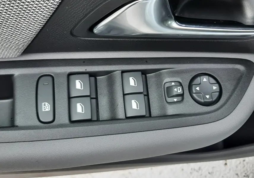 Gros plan sur la commande des vitres et rétroviseurs côté conducteur de la Citroën C4 blanche, version hybride 2026.
