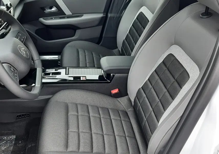 Vue intérieure côté gauche de la Citroën C4 2026, sièges bi-matière gris et noir avec console centrale brillante.