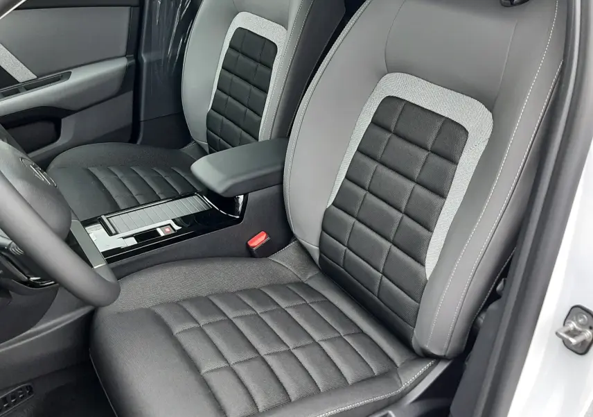 Vue intérieure côté conducteur de la Citroën C4 2026 blanc Okenite, sièges bi-matière gris et noir avec accoudoir central.