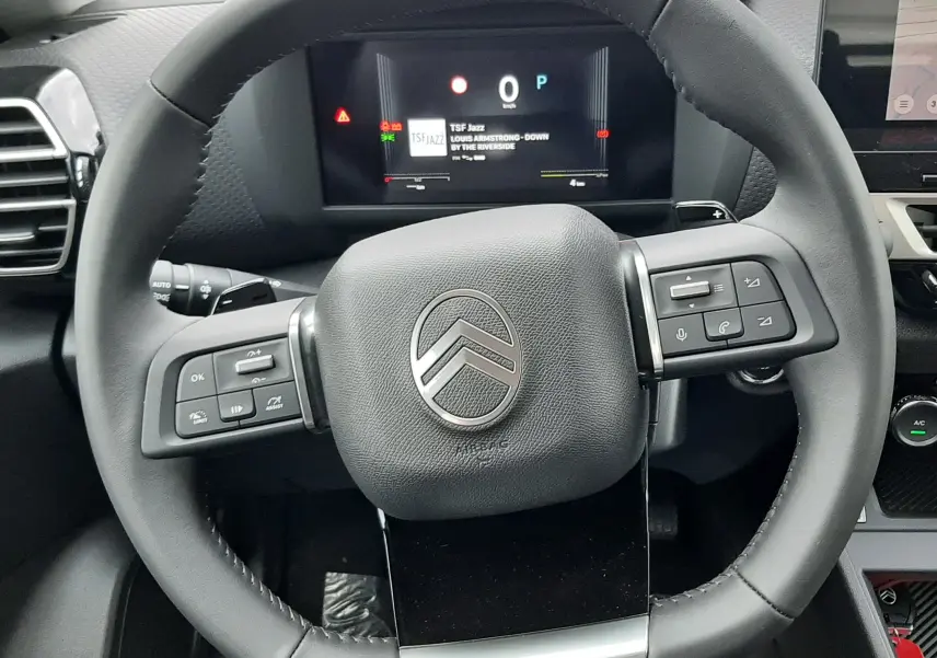 Vue rapprochée du volant noir de la Citroën C4 1.2 Hybrid 2026 avec tableau de bord digital affichant la radio TSF Jazz.