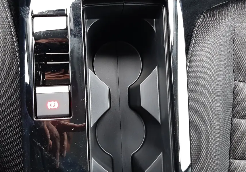 Gros plan sur la console centrale noire avec porte-gobelets et bouton frein à main électrique dans une Citroën C4 hybride.