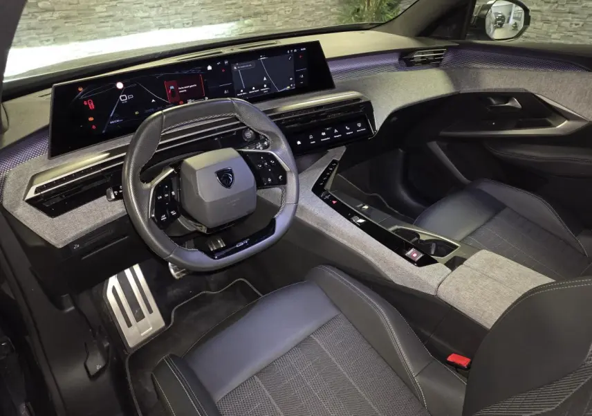Vue intérieure côté conducteur du Peugeot 5008 gris 2025, avec tableau de bord numérique panoramique et volant compact cuir.