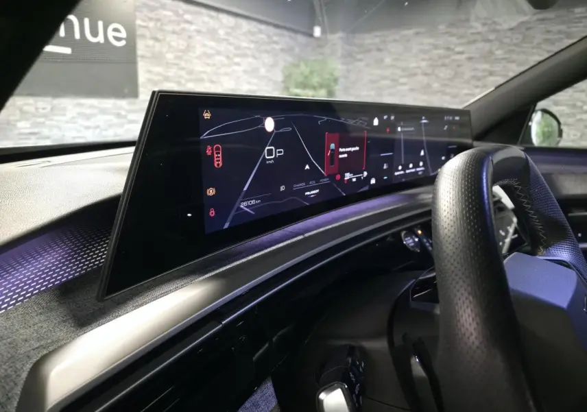 Vue intérieure du tableau de bord et écran numérique panoramique du Peugeot 5008 gris hybride, avec volant perforé noir.