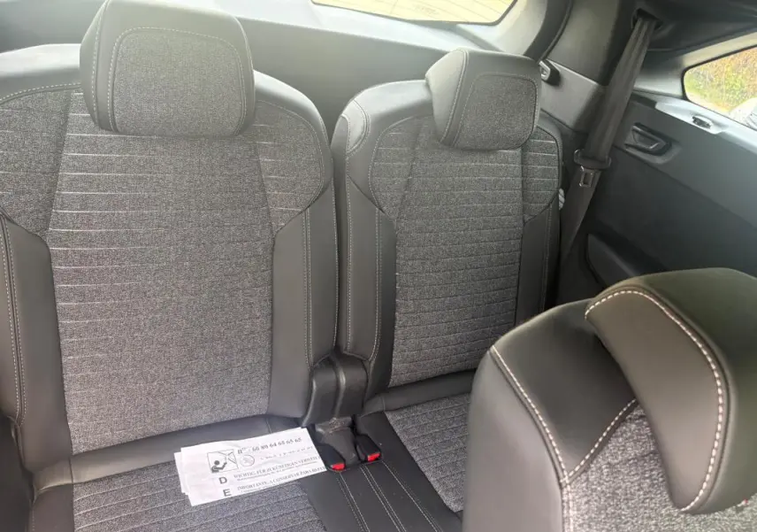 Vue intérieure sur les sièges arrière du Peugeot 5008 Hybrid 2025, tissu gris et cuir noir avec surpiqûres blanches.