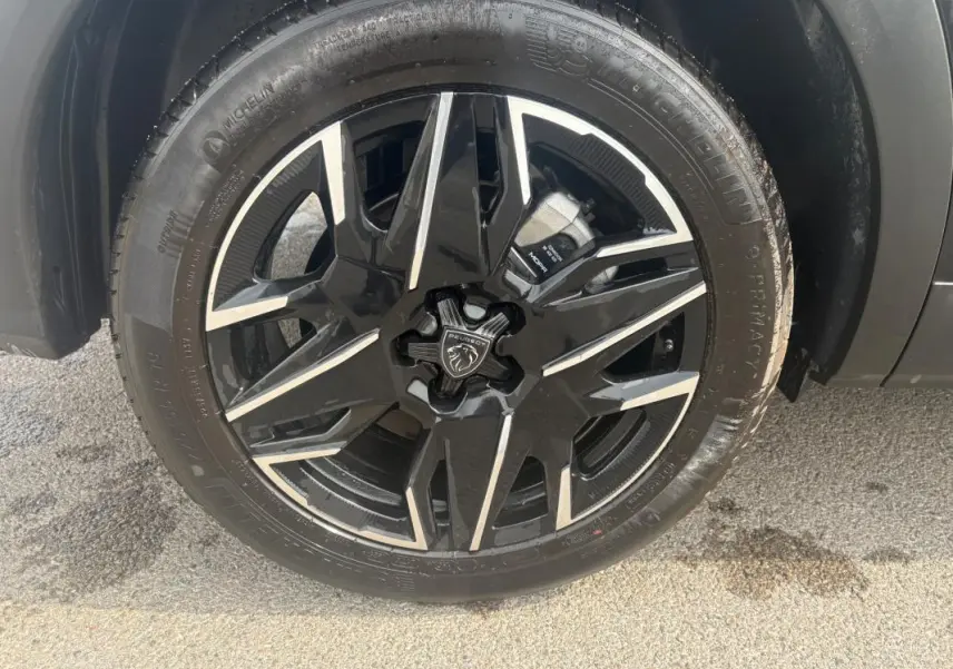 Gros plan sur la roue avant gauche du Peugeot 5008 noir 2025, avec jante alliage noire et argentée distinctive.