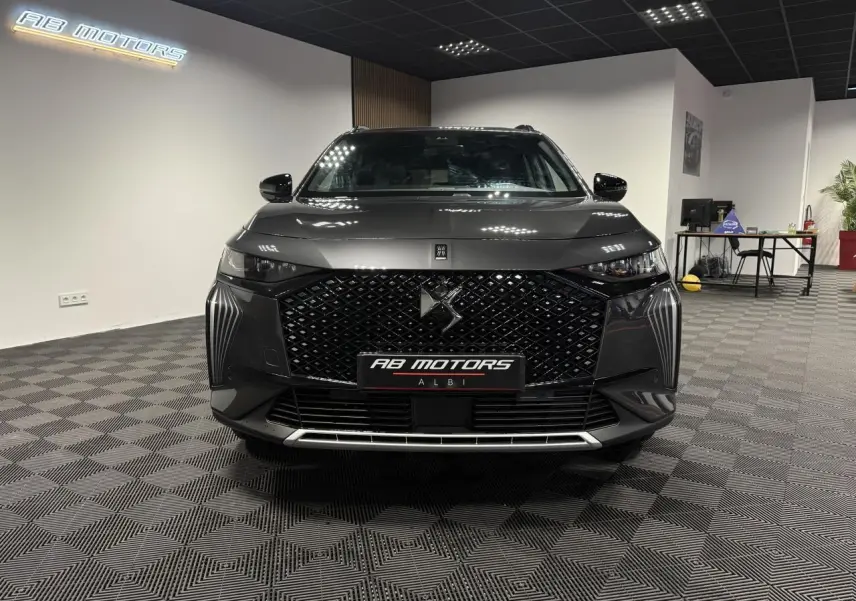 Vue avant d'un DS7 Crossback gris métallisé avec calandre noire à motifs losanges et logo DS central, en showroom.