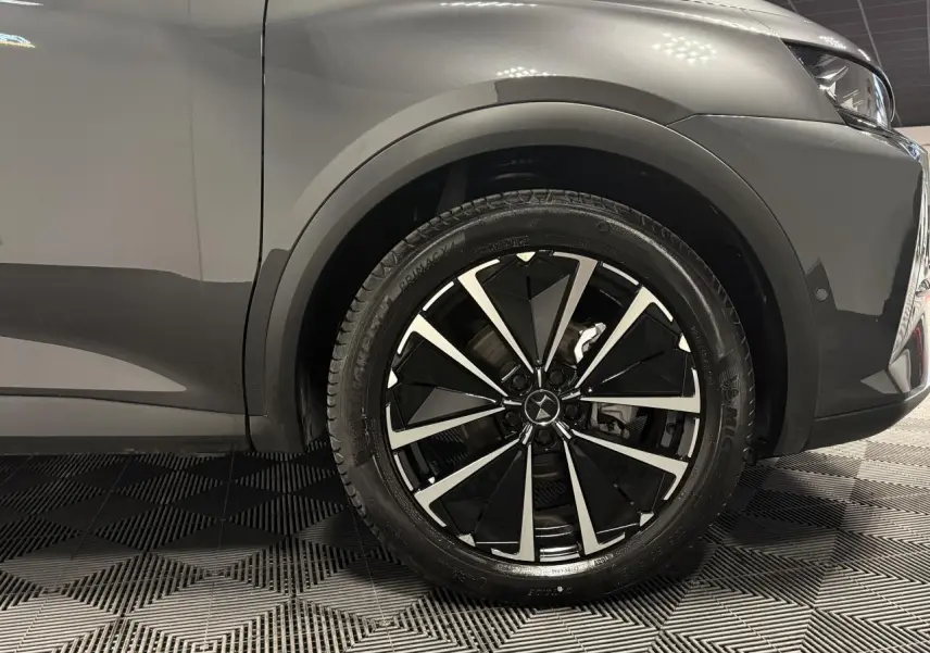 Gros plan sur la roue avant droite du DS7 Crossback gris, avec jante alliage noire et argentée au design moderne.
