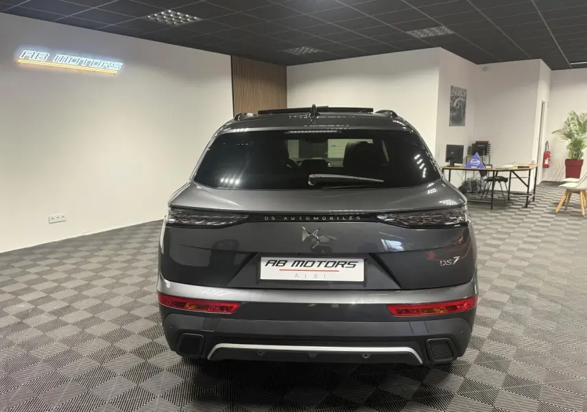 Vue arrière du DS7 Crossback gris métallisé 2025 avec feux arrière 3D et logo DS Automobiles visible en showroom.