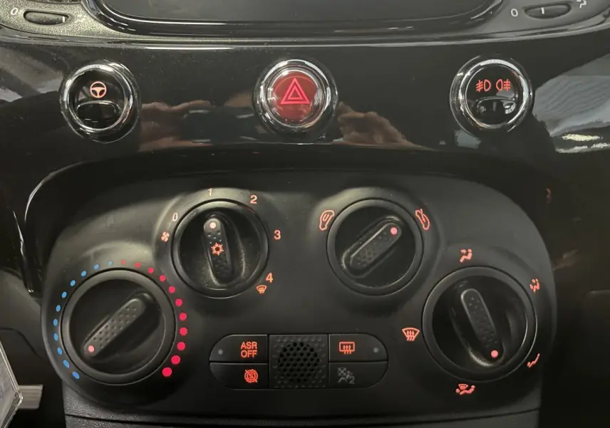 Commandes de climatisation et boutons de sécurité en gros plan sur la planche de bord noire de la Fiat 500 Dolcevita 2023.