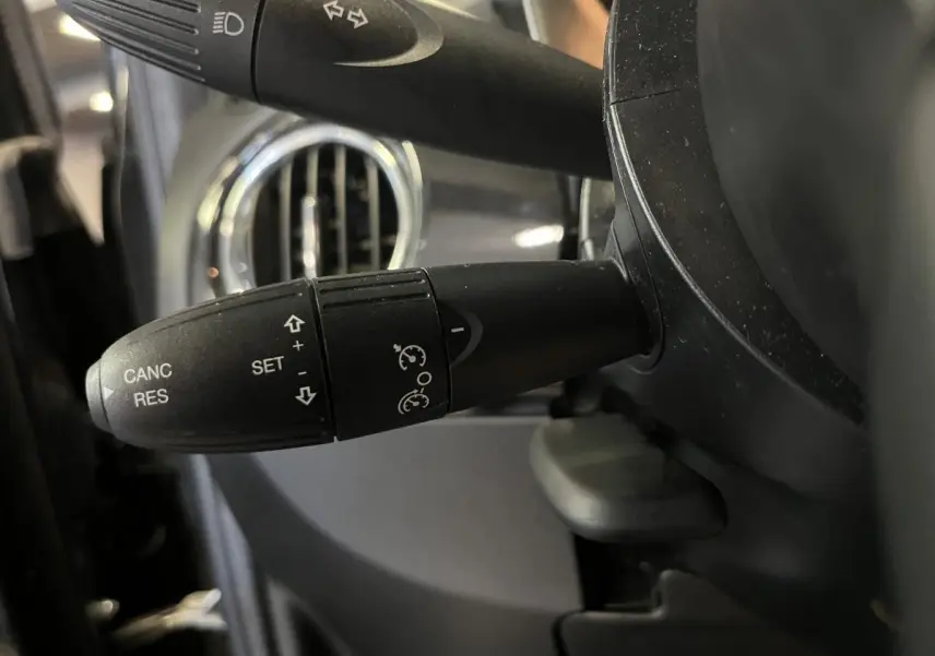 Gros plan sur la commande de régulateur de vitesse noire, avec volant et aérateur chromé d'une Fiat 500 noire 2023.